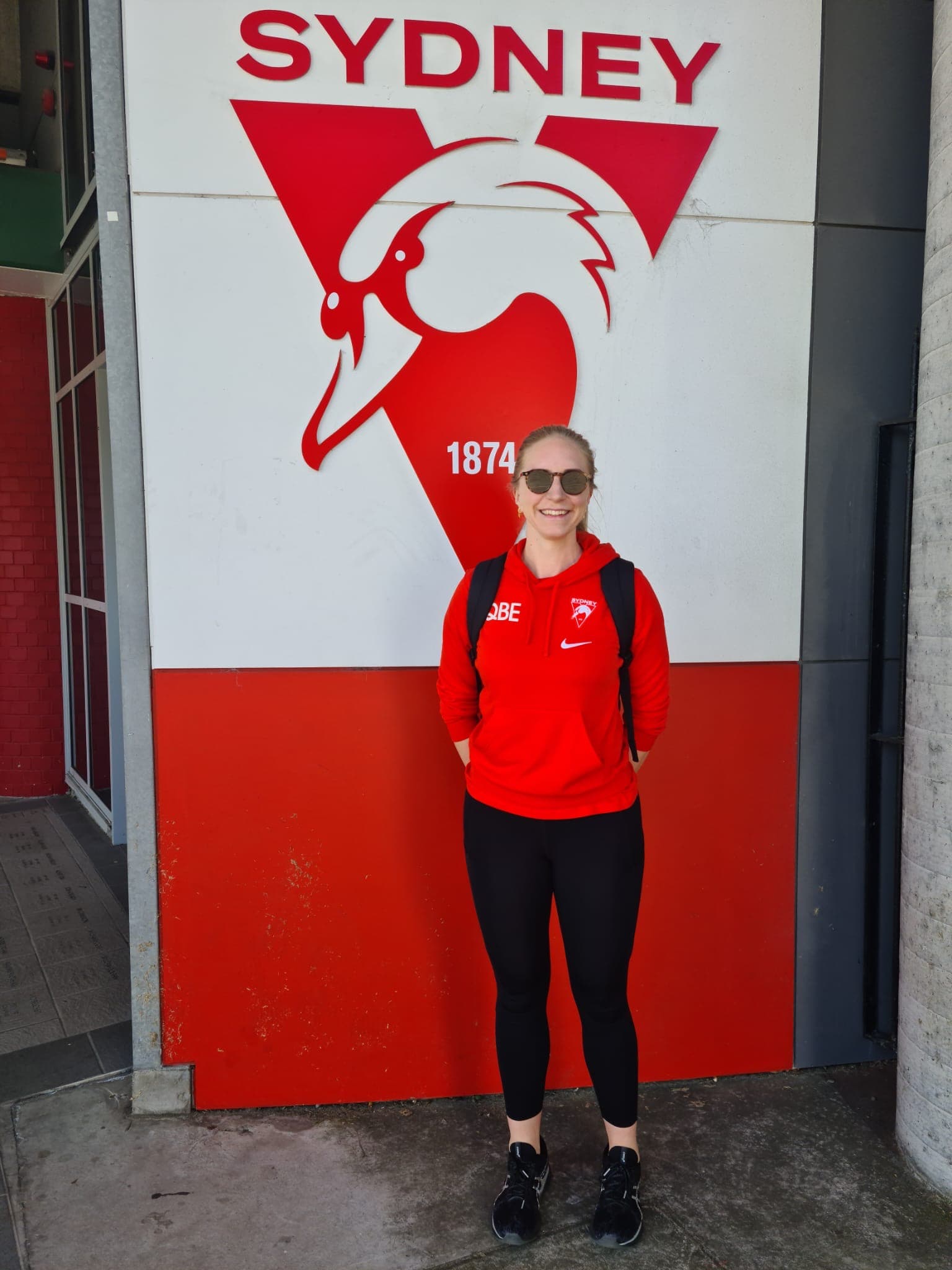 Eimear Keane in a Sydney Swans hoodie, standing in front of the Swans crest at the stadium