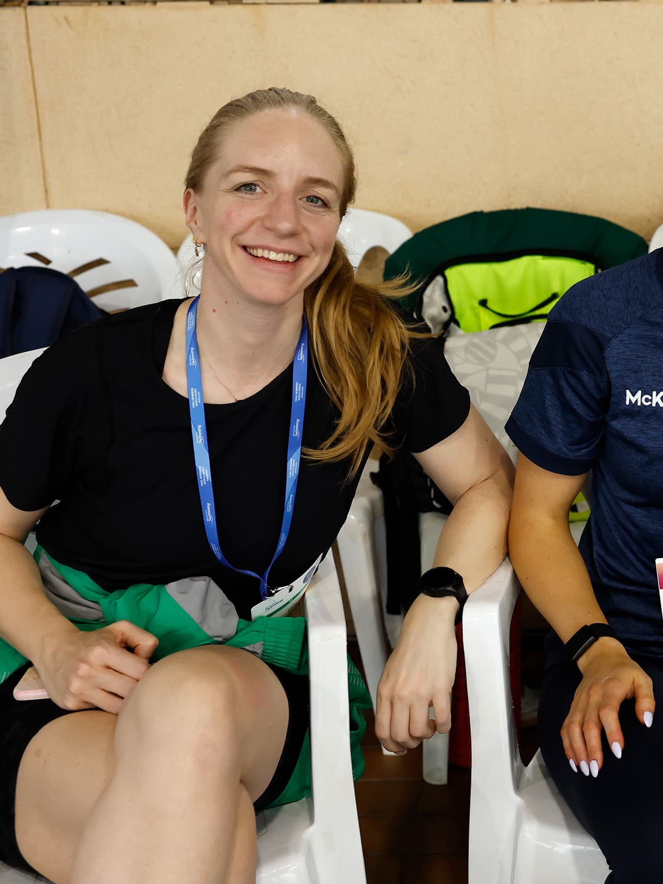 Eimear Keane seated between two Team Ireland colleagues in staff polos at a Paralympic competition venue, all three smiling at the camera